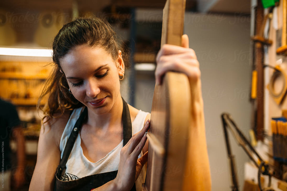 Young Woman Luthier holding a guitar template while looking at c
