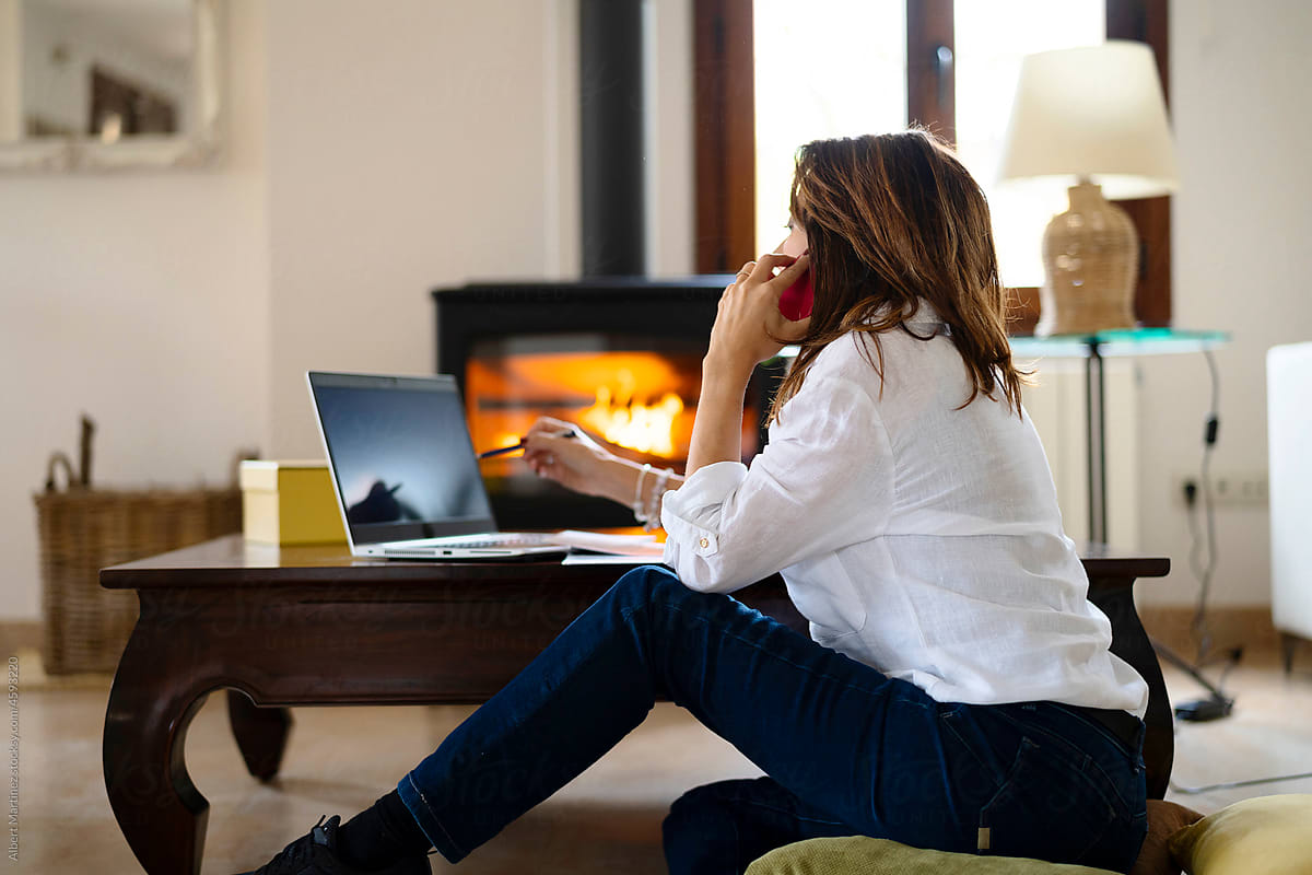 Female freelancer speaking on cellphone by the fireplace