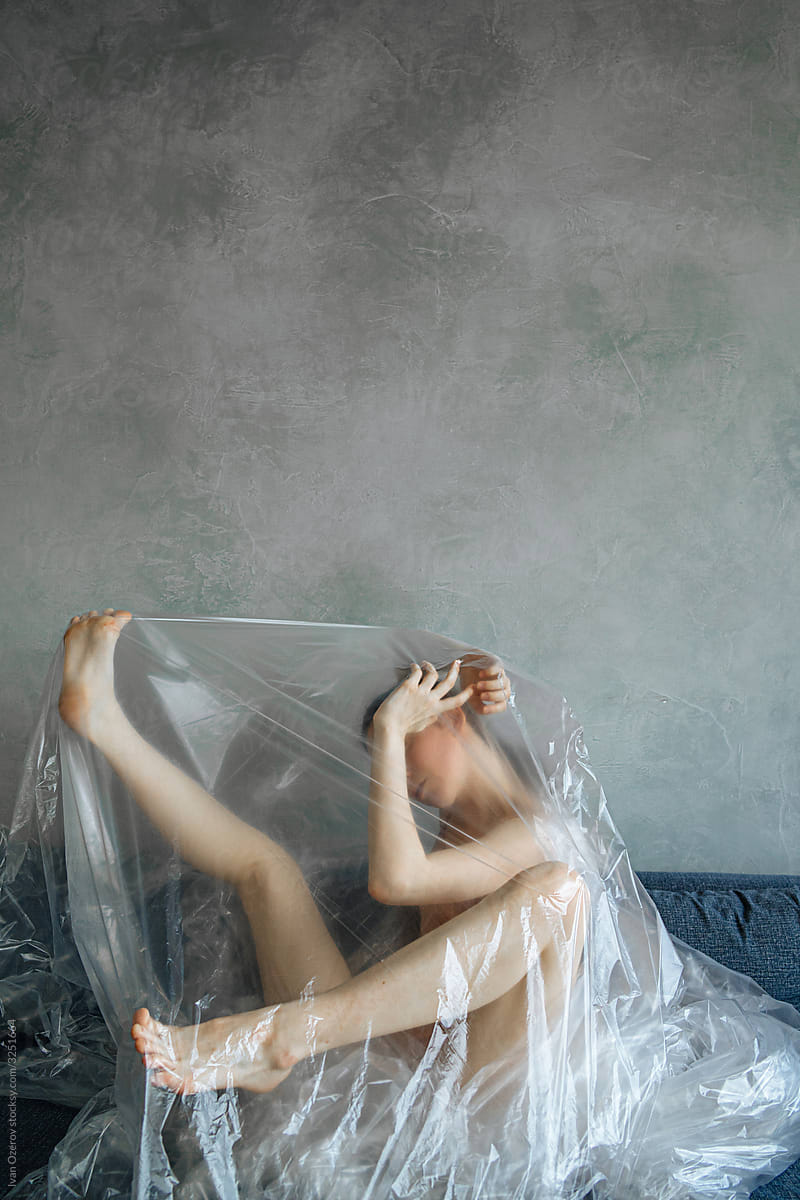 naked girl wrapped in cellophane sits on the couch