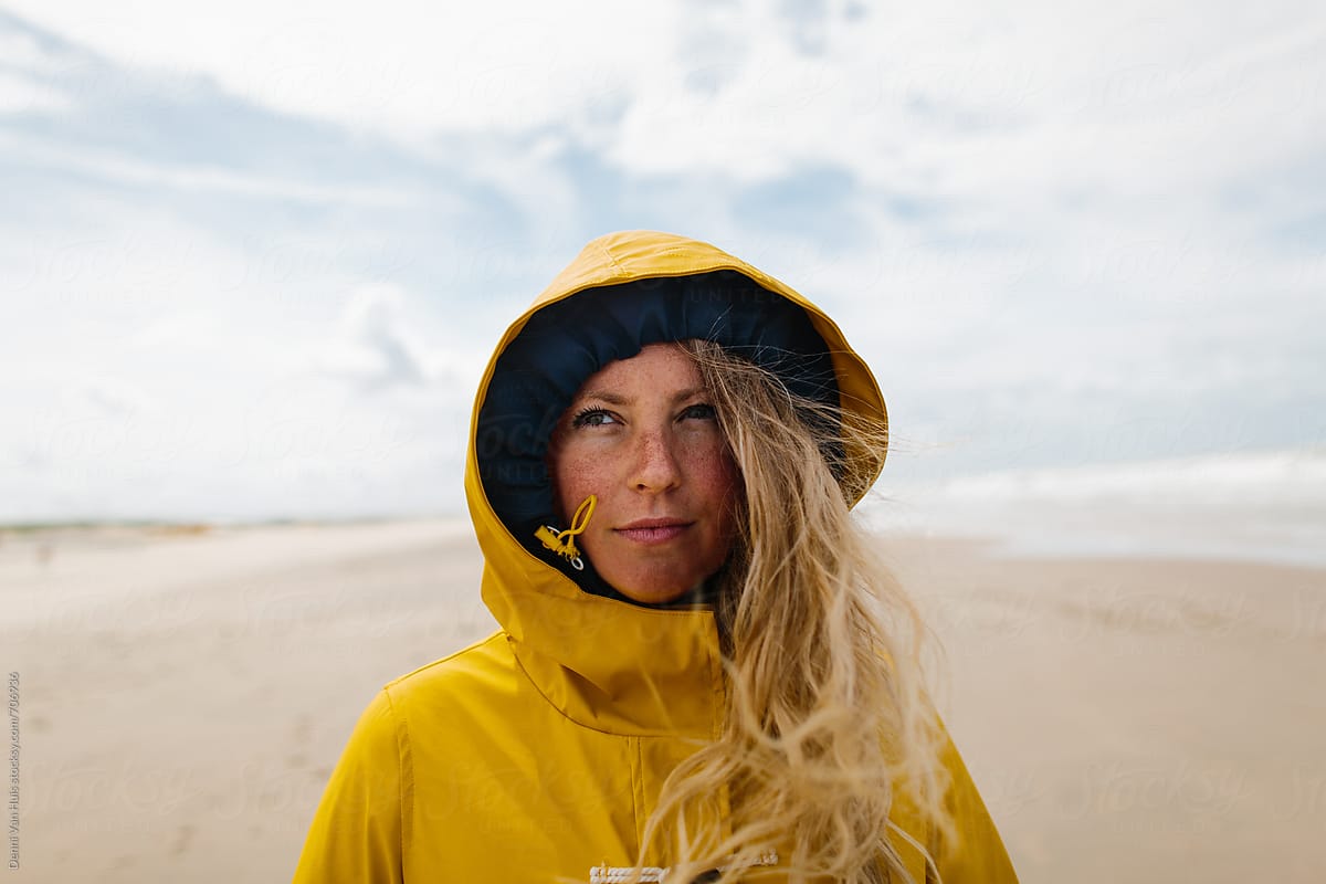 Woman on a windy beach wearing a yellow raincoat.