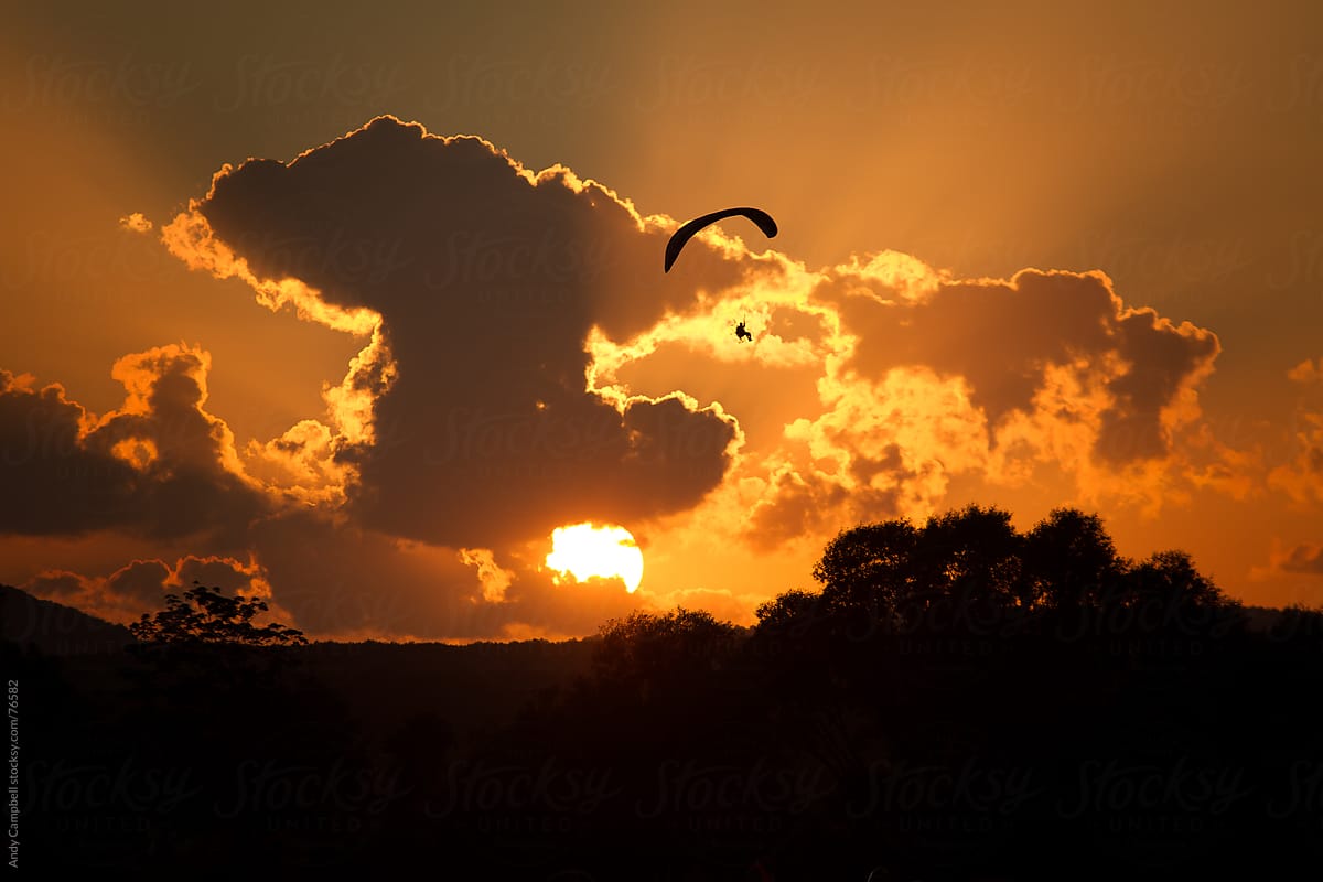 An adventurous paraglider pilot flying into the sunset
