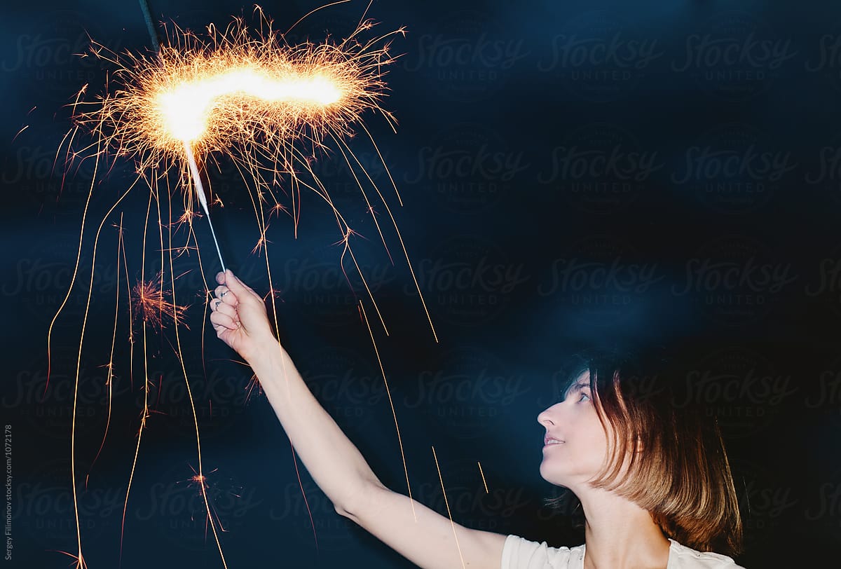 Woman posing with burning sparkler in night