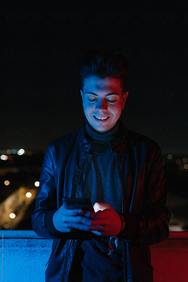 Smiling guy chatting on smartphone on balcony at night