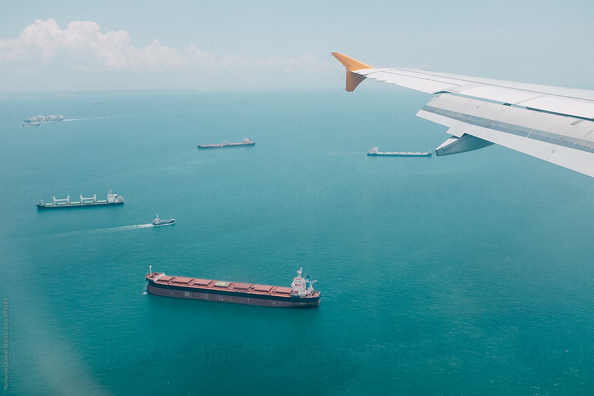 Commercial Airplane Flying over Sea Full of Cargo Ships