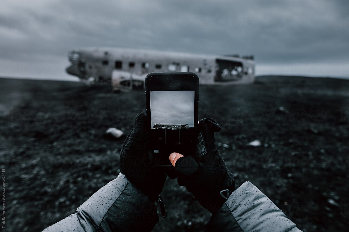 man taking a photo with his phone to the crashed Navy Douglas Super DC-3 plane in Vik, Iceland