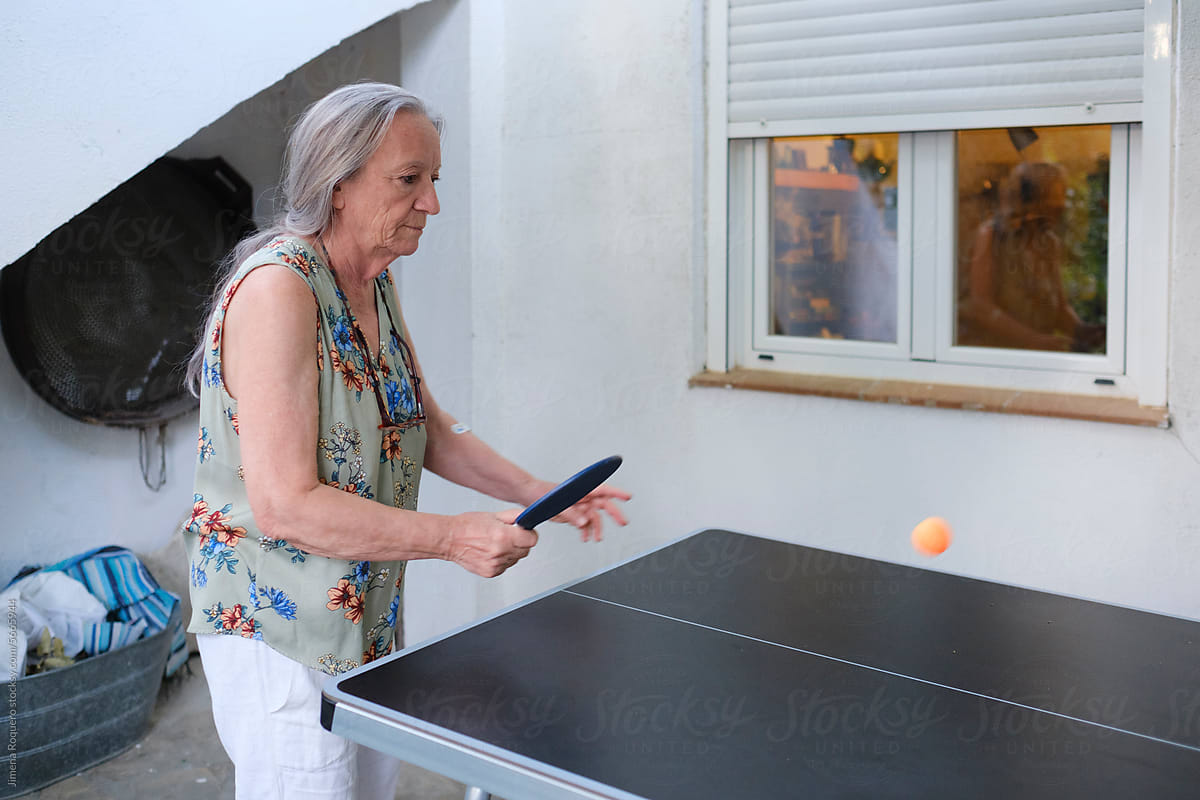 Senior woman playing ping pong in rural house patio