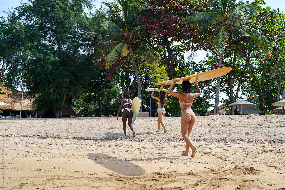 Female surfers carrying surfboards on sandy beach