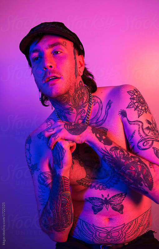 Potrait of a young heavily tattooed punk man with pink and blue studio lighting