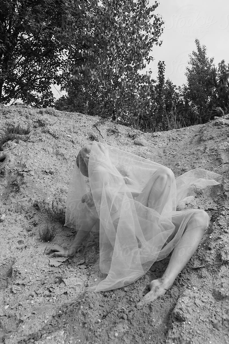 black and white photo of a girl sitting on the beach on a mountain, throwing a light cloth over herself
