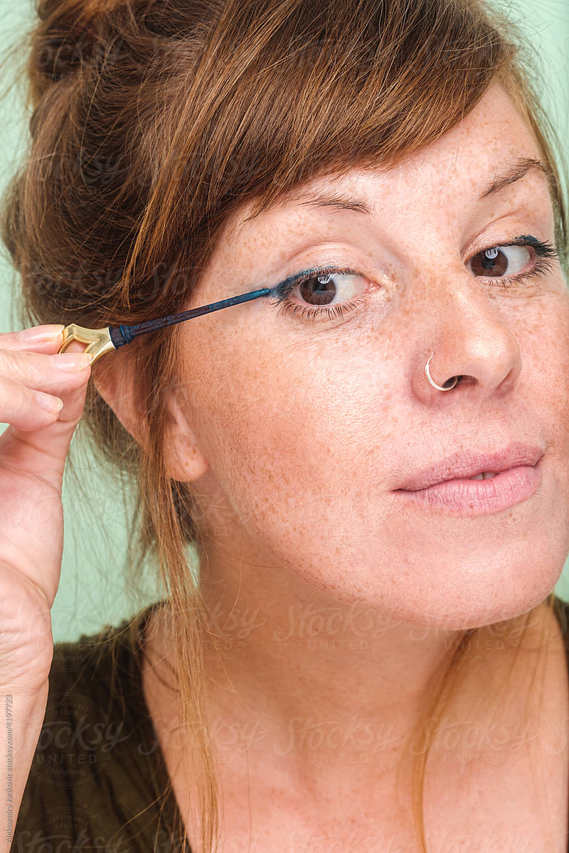 Close Up Of A Woman With Freckles Applying Eyeliner
