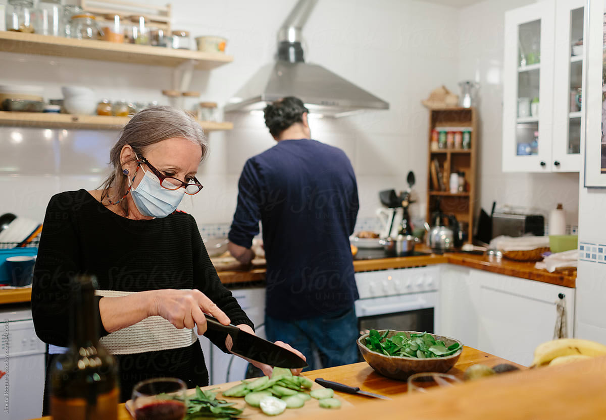 Elderly woman with face making salad in home kitchen.