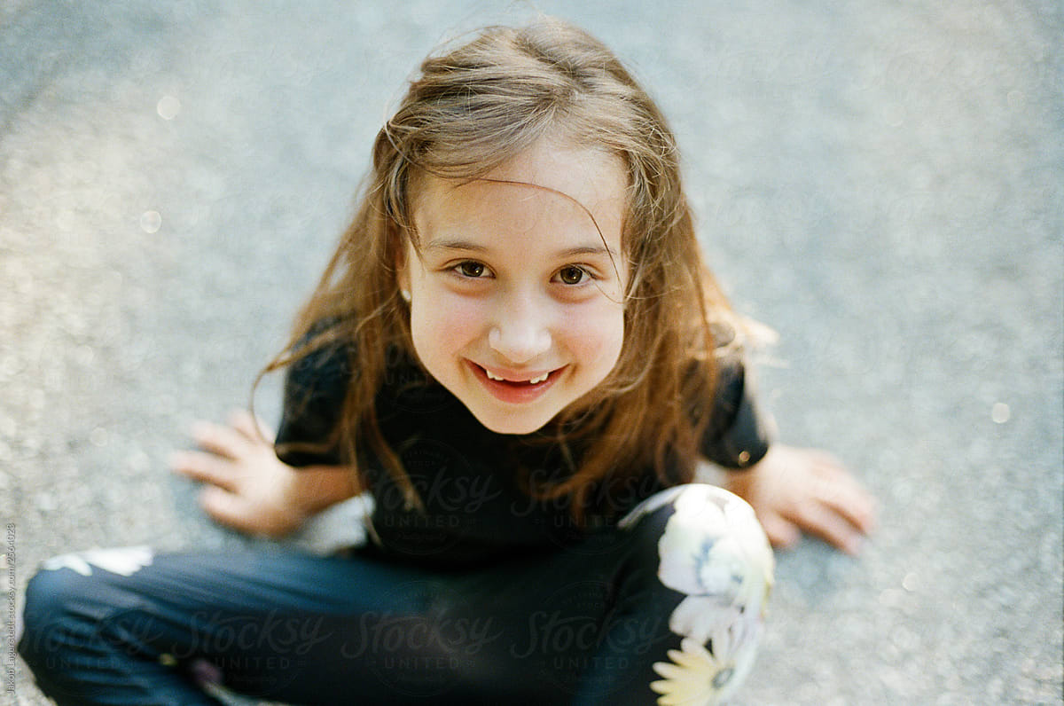 Portrait Of A Young Happy Girl Sitting On Patch Of Asphalt By Stocksy