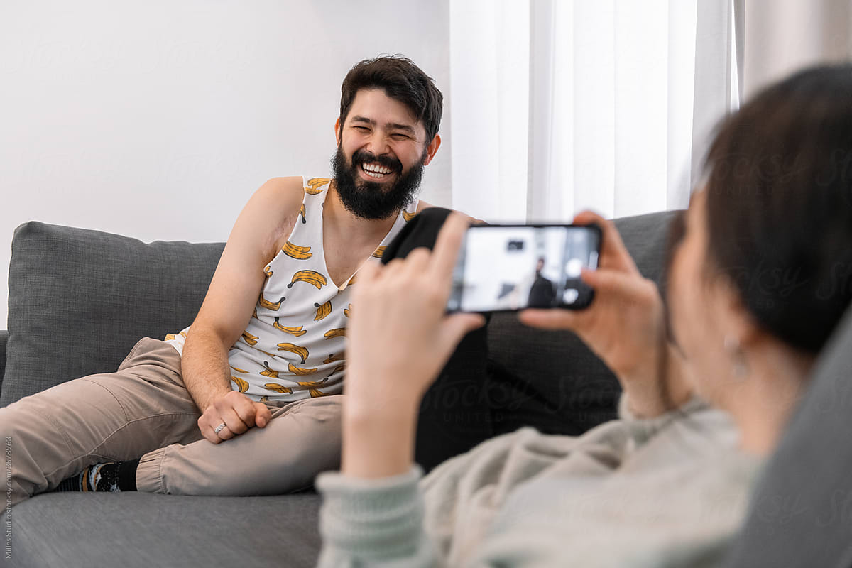 Woman taking photo of laughing man on couch
