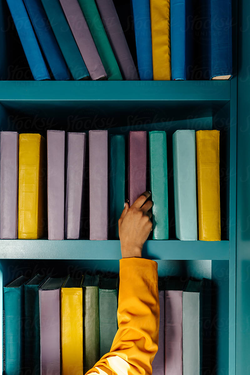 Anonymous person in yellow jacket choosing book from shelf