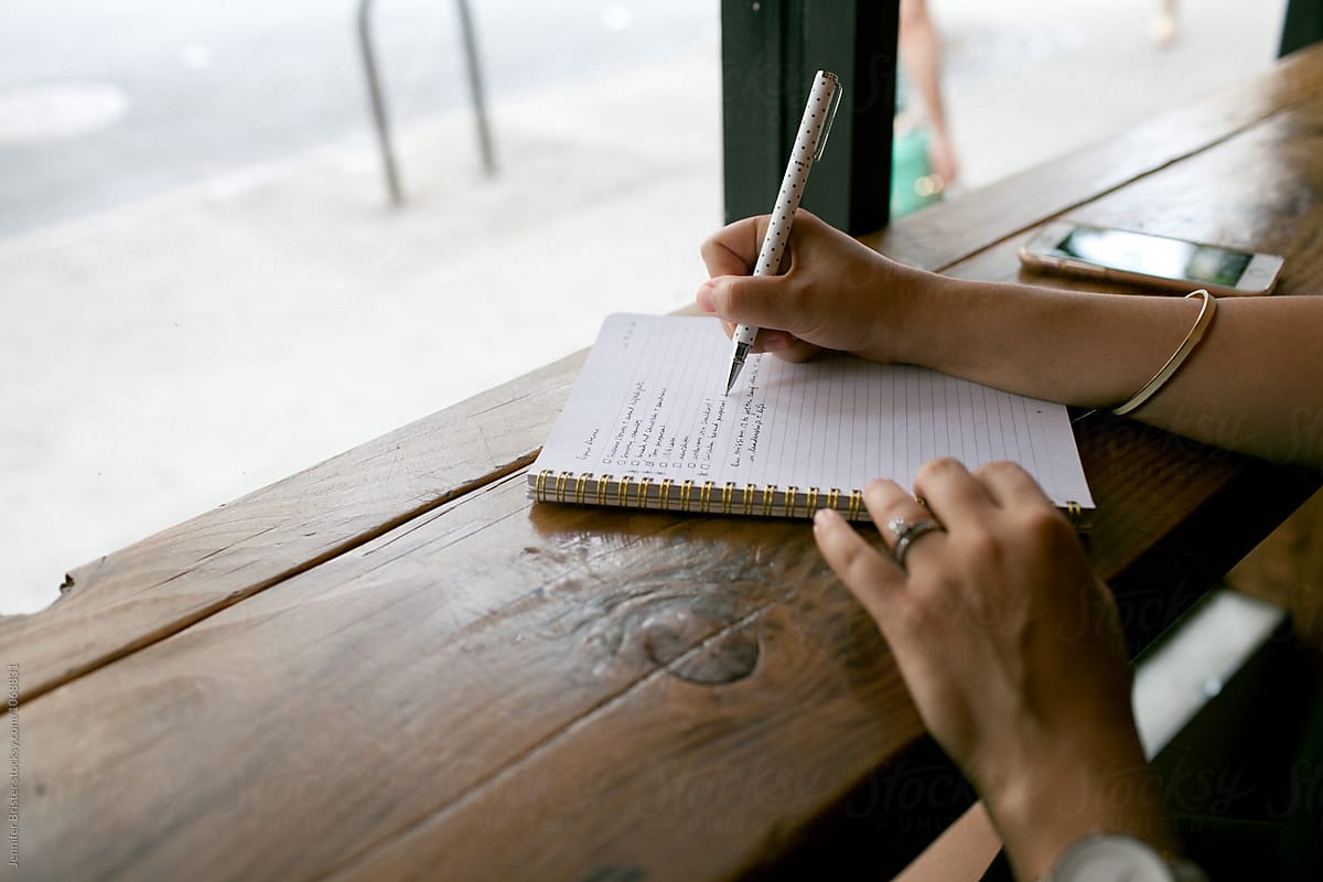 A woman's hand writing out list in notebook