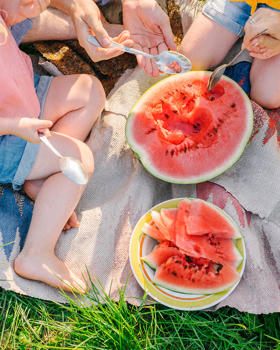 Unrecognizable people eat watermelon with a spoon in the park