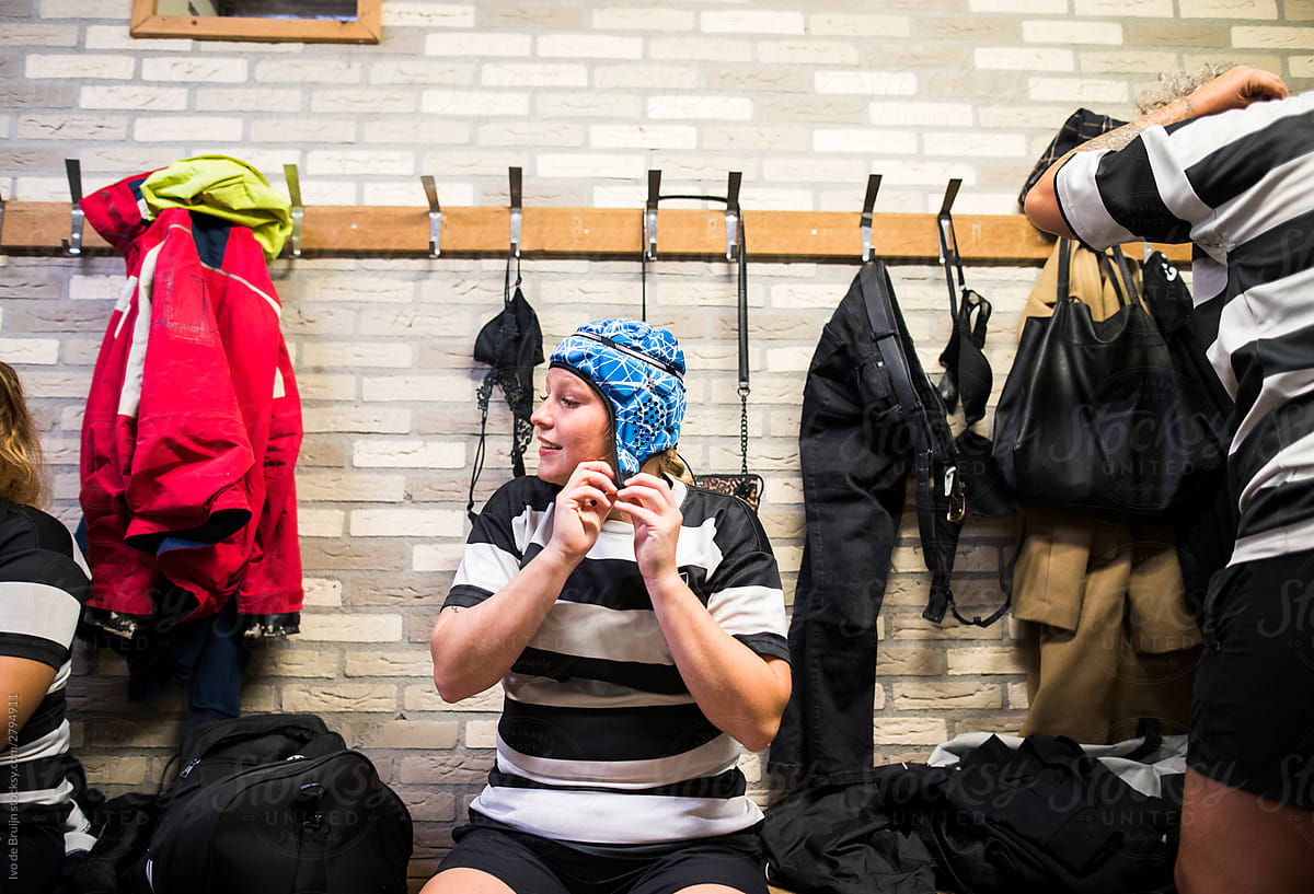 A female rugby player putting on her scrum cap, sitting in the d