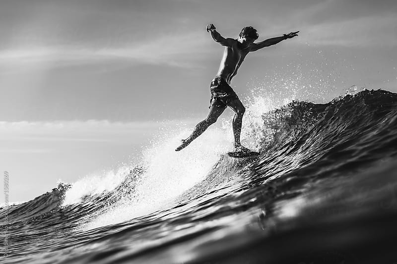 Silhouette of man in the ocean surfing wave in bright day light. Stylish pose. Black and white image.