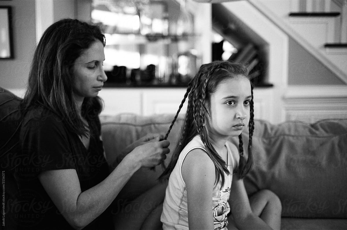 Mother braiding her daughter\'s hair while she watches television