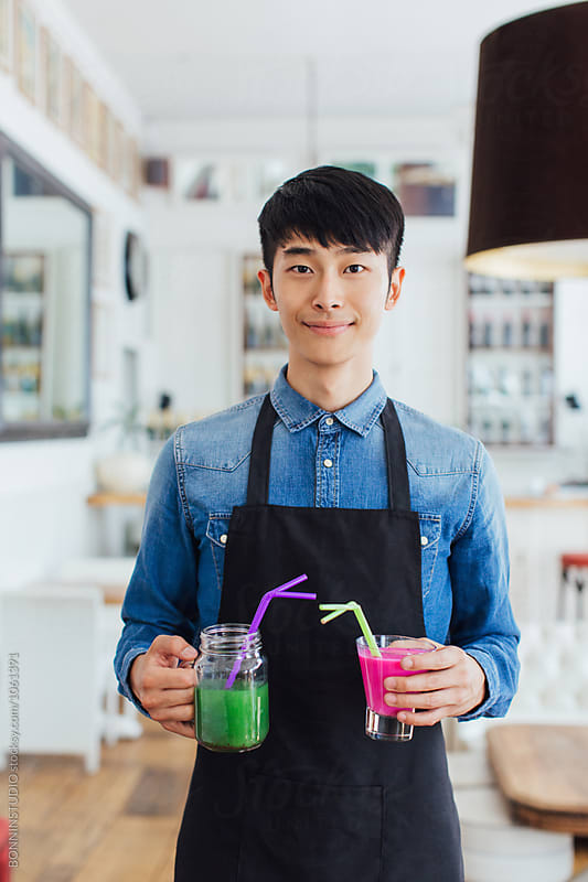 Portrait of an asian waiter serving colorful fresh smoothies in a restaurant.