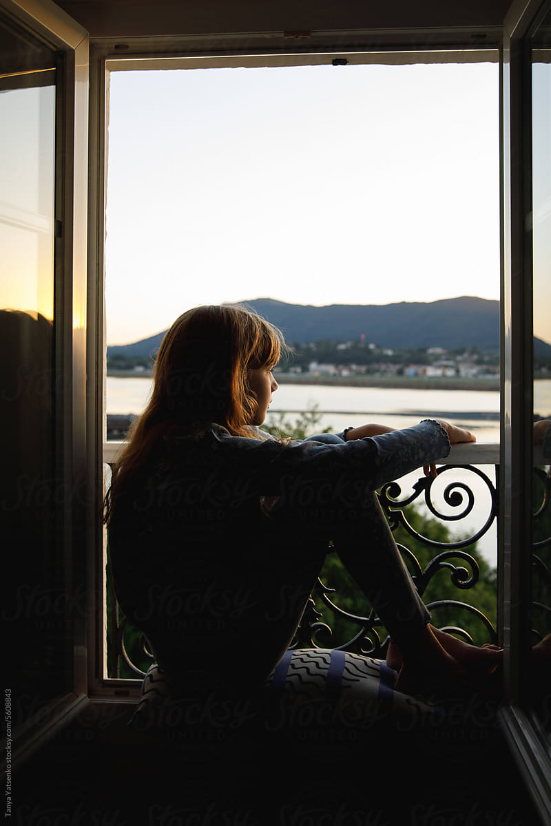 A girl sitting on the window frame during twilight