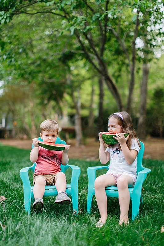 Cute young boy and girl eating watermelon under a tree