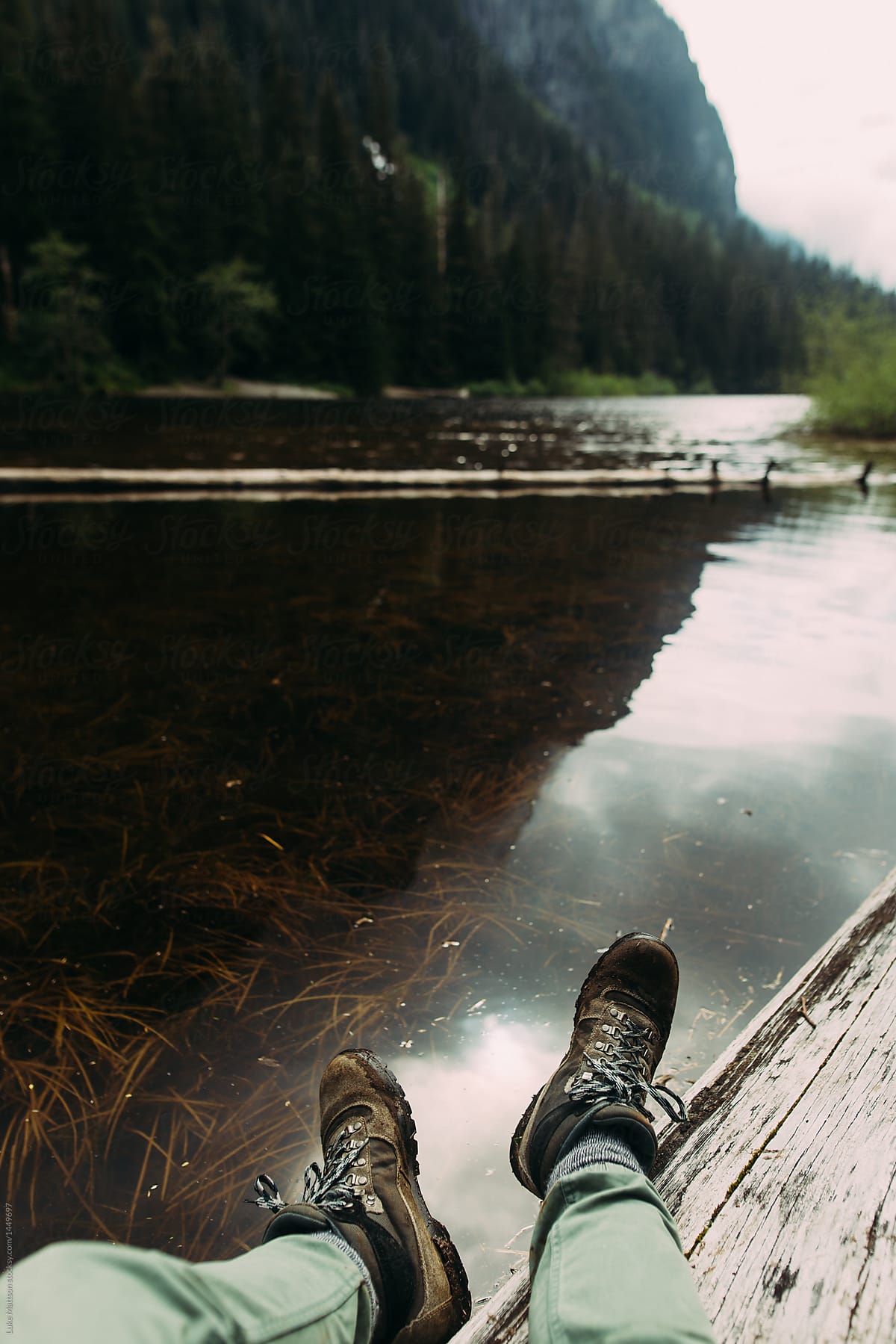 Hiker Dangling Legs Off Log Over Reflective Lake Surface