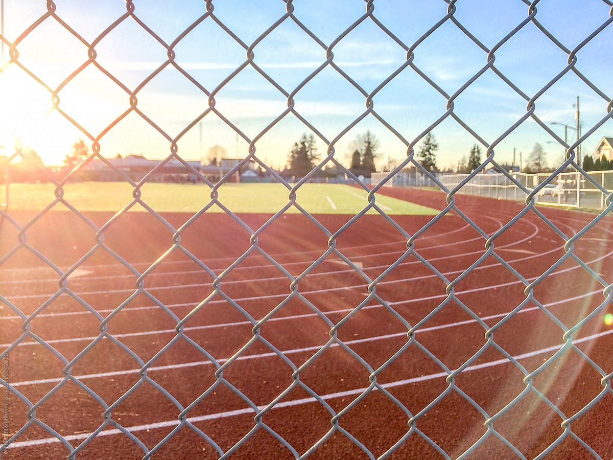 Athletic running track seen through chainlink fence at sunset
