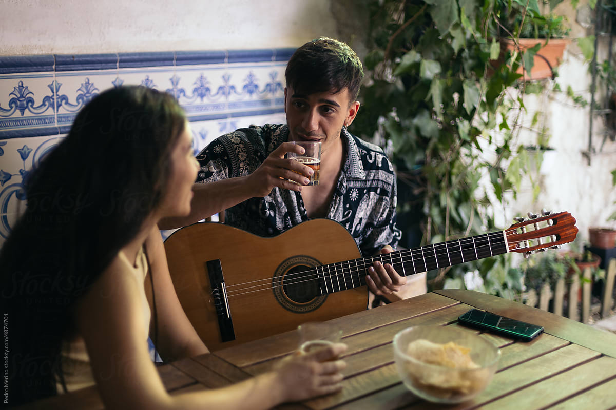 Young man playing the Spanish guitar in a patio with his friend