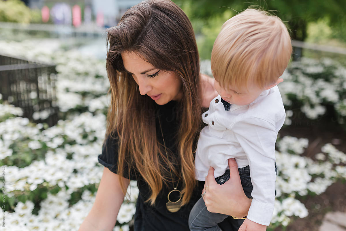 Young, cool mom holding her son while picking flowers