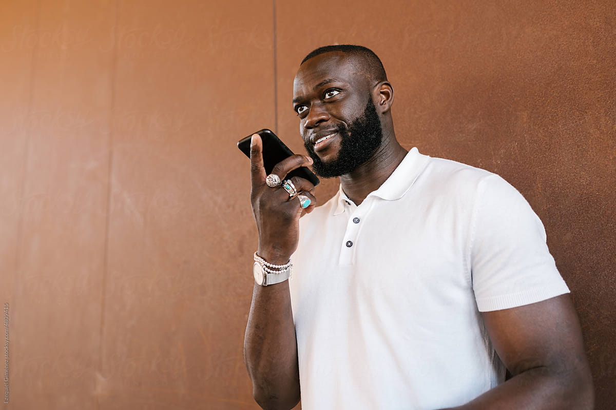 Smiling black guy recording voice message on smartphone