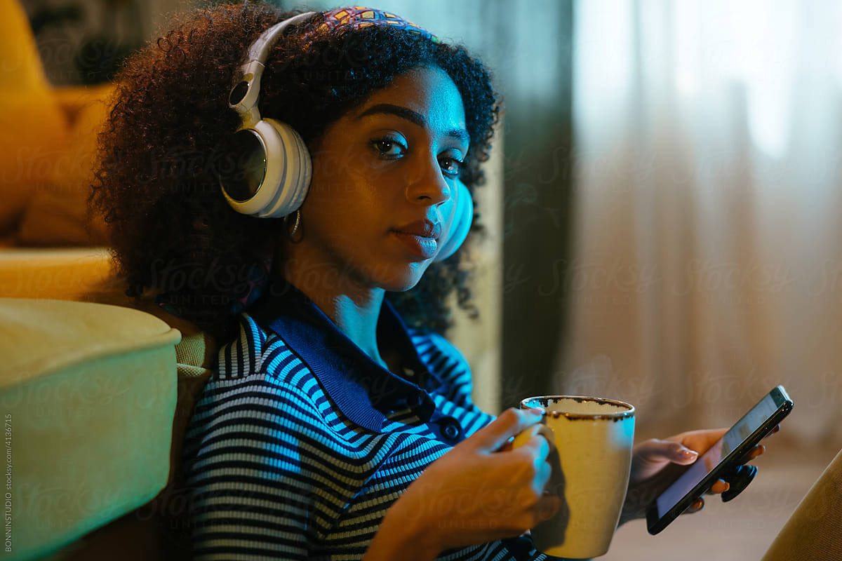 Black woman in headphones with smartphone and coffee
