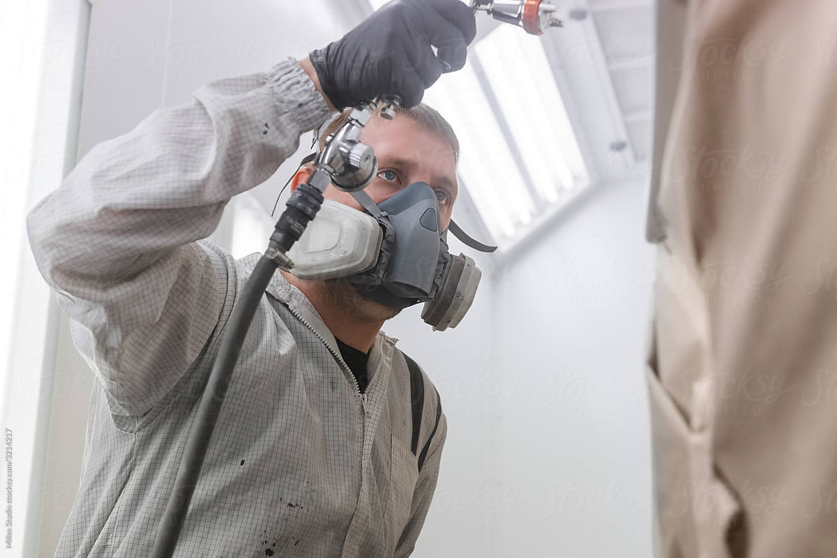 Professional technician in respirator painting car