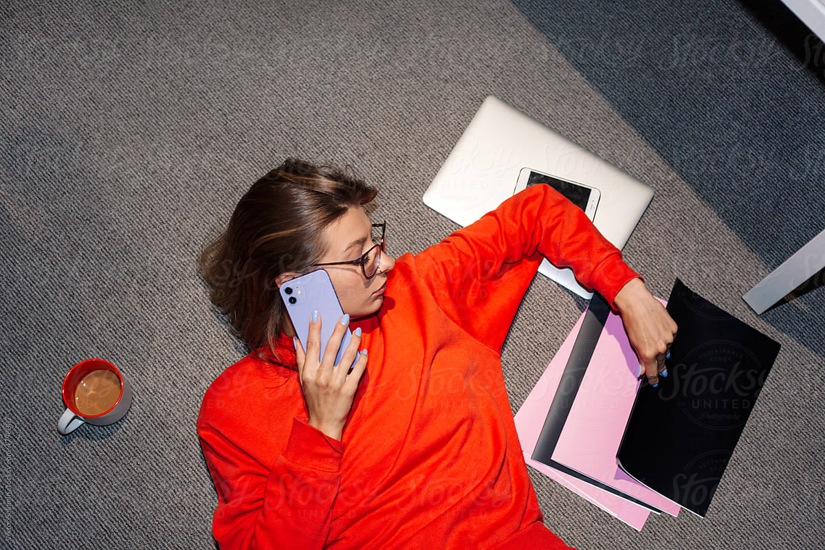 Young woman talking on smartphone looking at documents in office