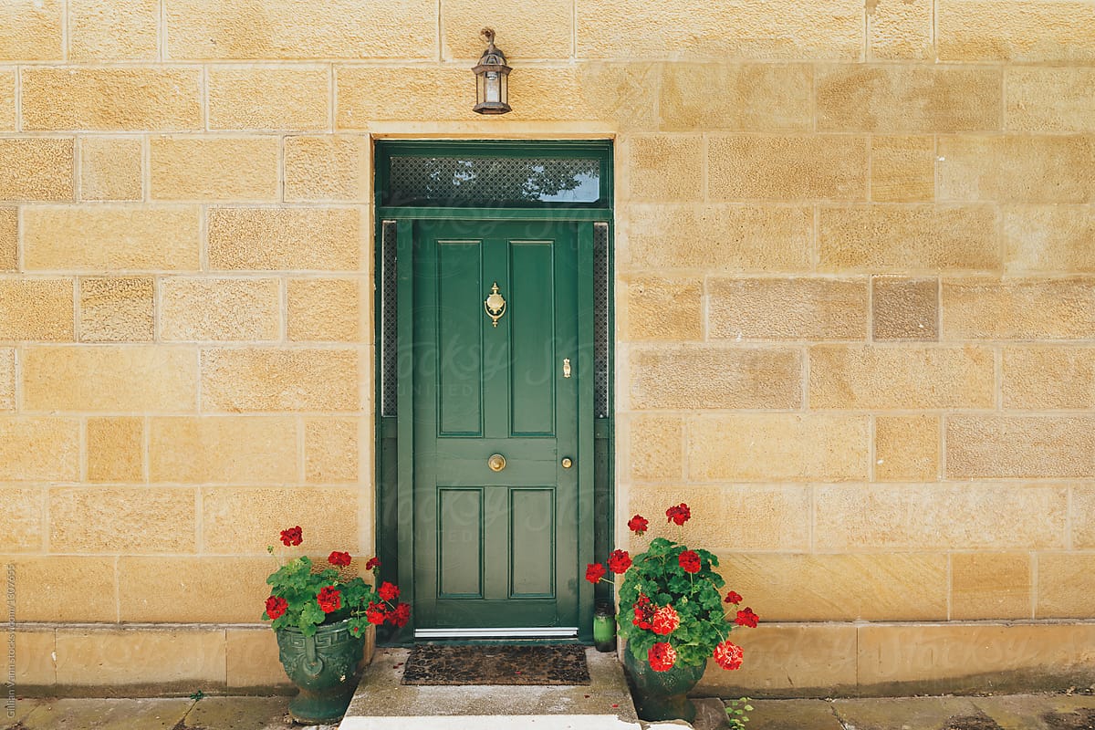 green door in a stone wall with potted red geraniums