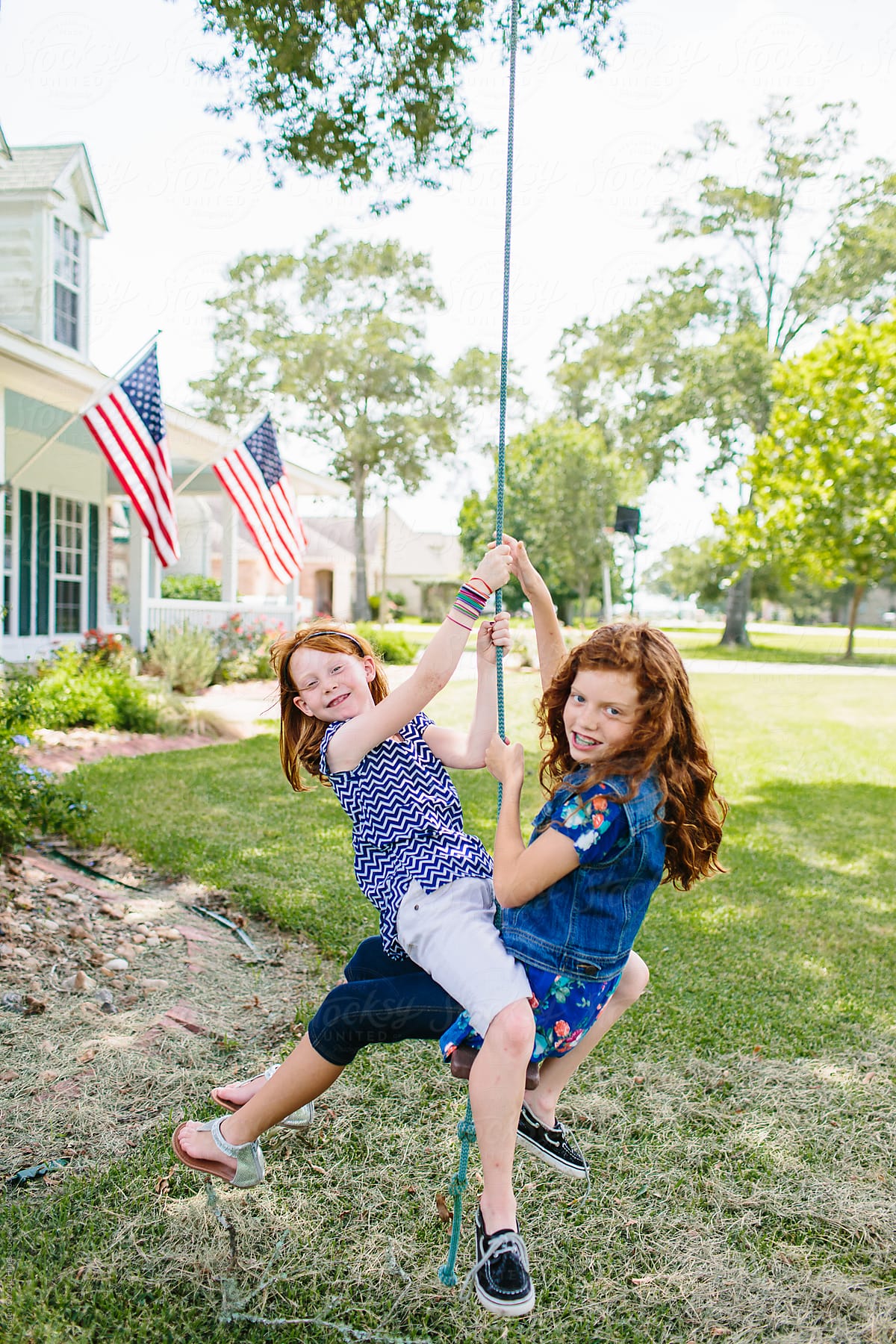 Two red headed sisters sharing a rope tree swing