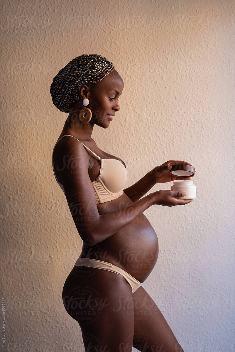 Sensual black pregnant woman opening jar with cream