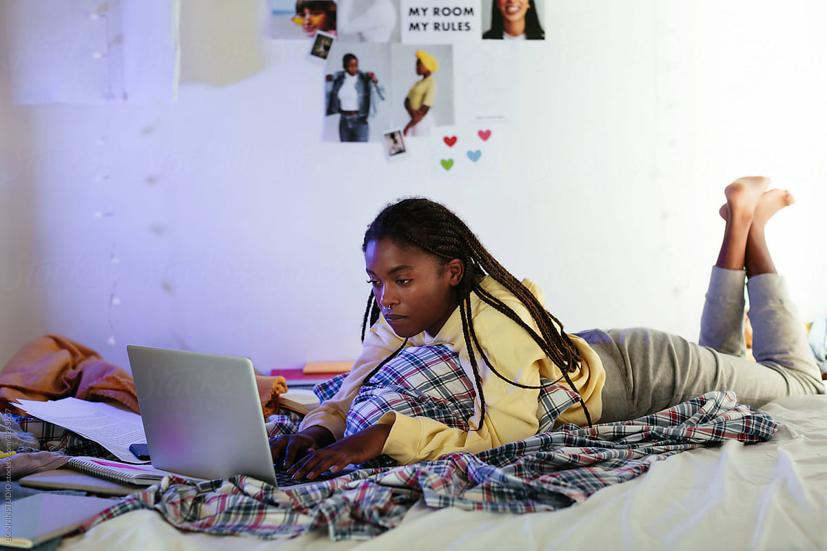 Black teen student using laptop on bed