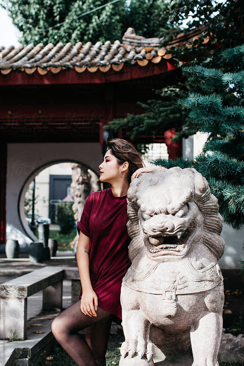 Charming young woman posing near the asian looking creature statue in the street