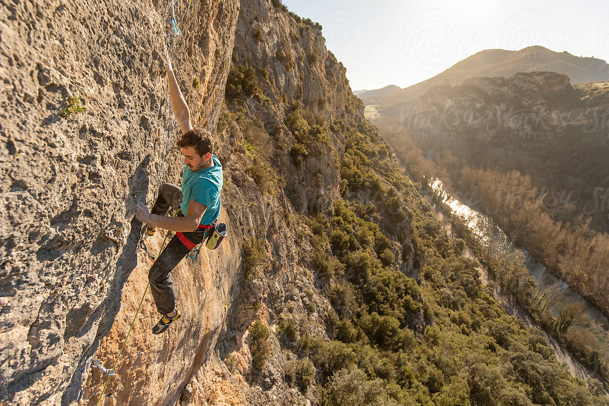 Rock climber climbing a mountain cliff at sunrise