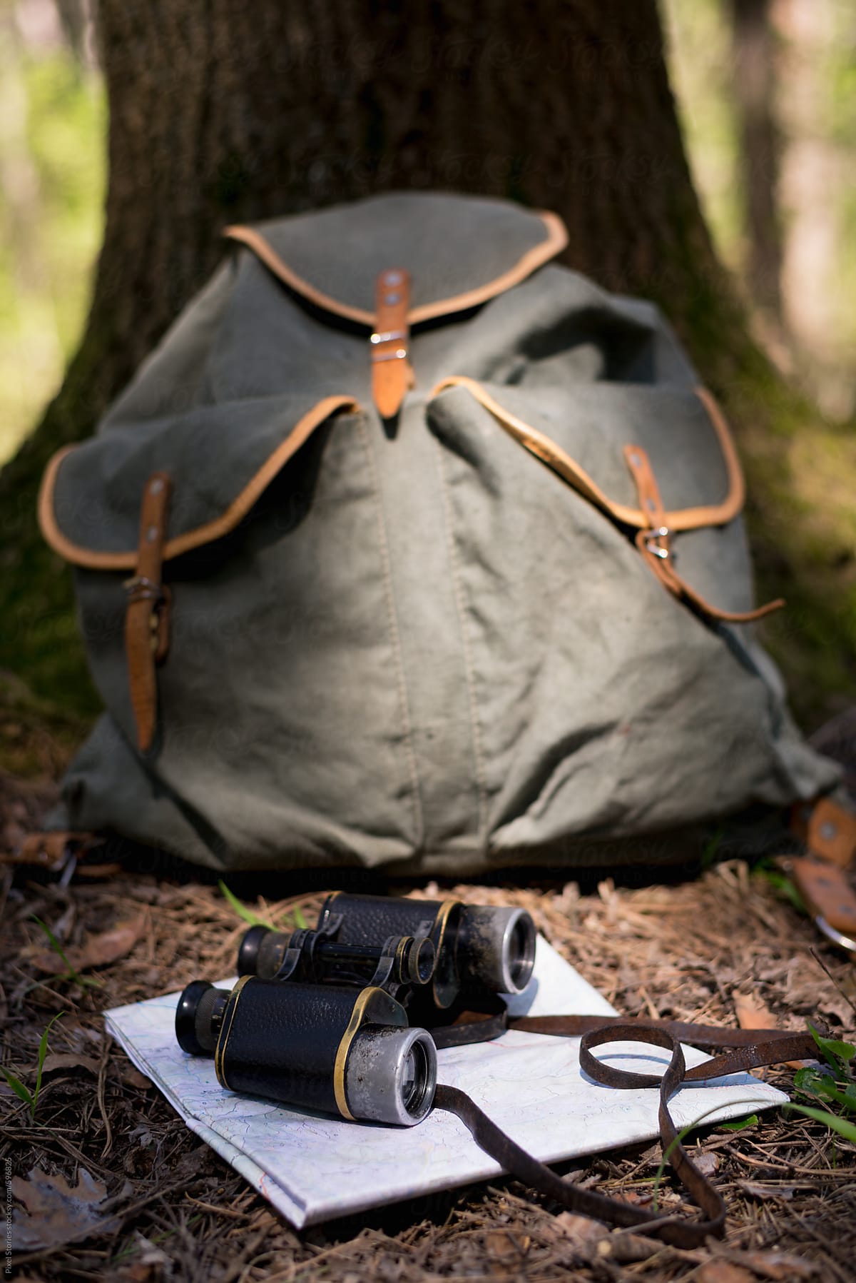 Vintage backpack, old binoculars and map next to a tree