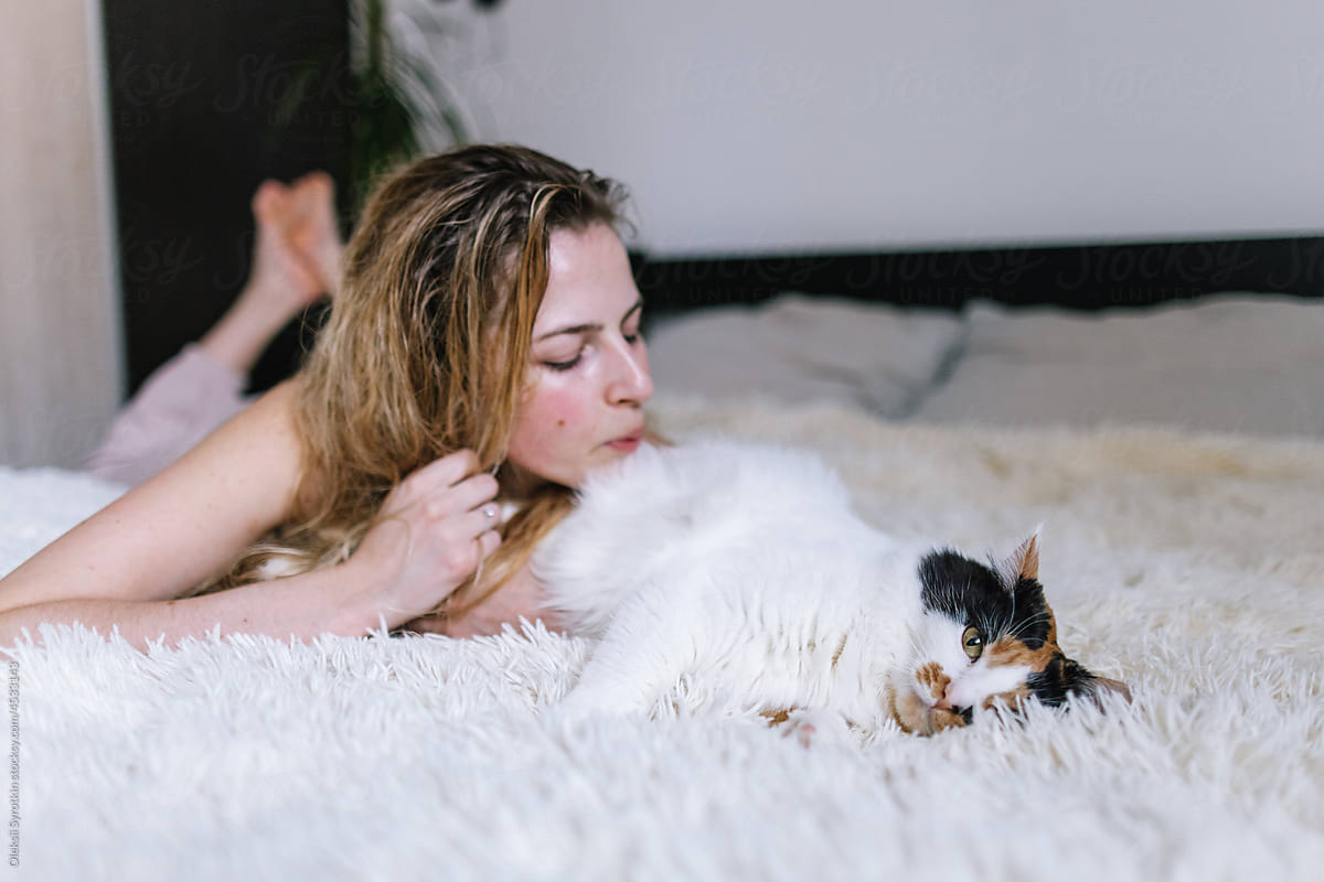 Cute girl touching fur of cat by lips while lying on bed