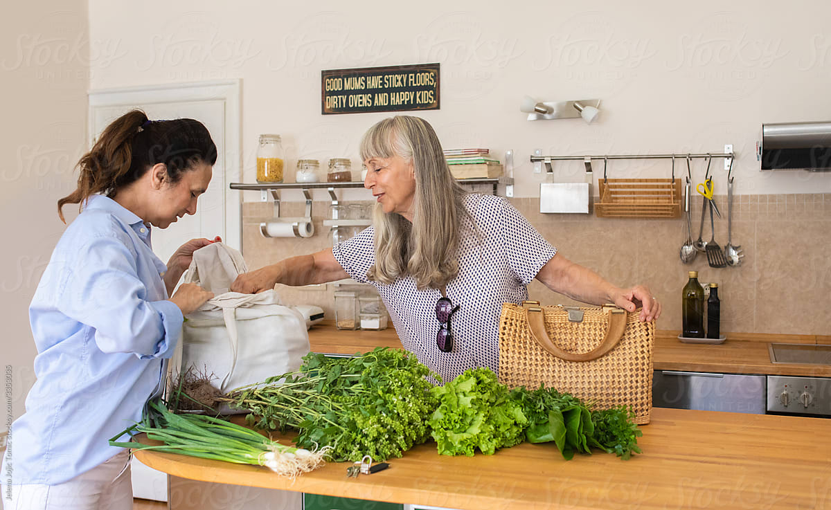 Two elderly women at home unpack the fresh groceries from the market