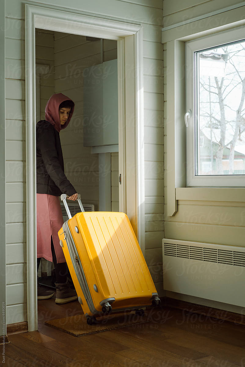 Young woman rolls out a large yellow plastic travel suitcase
