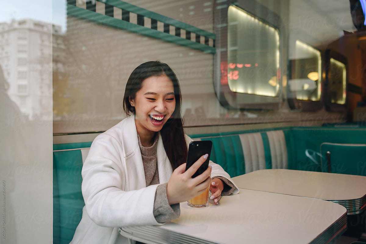 Happy young Chinese woman using a mobile in a coffee shop