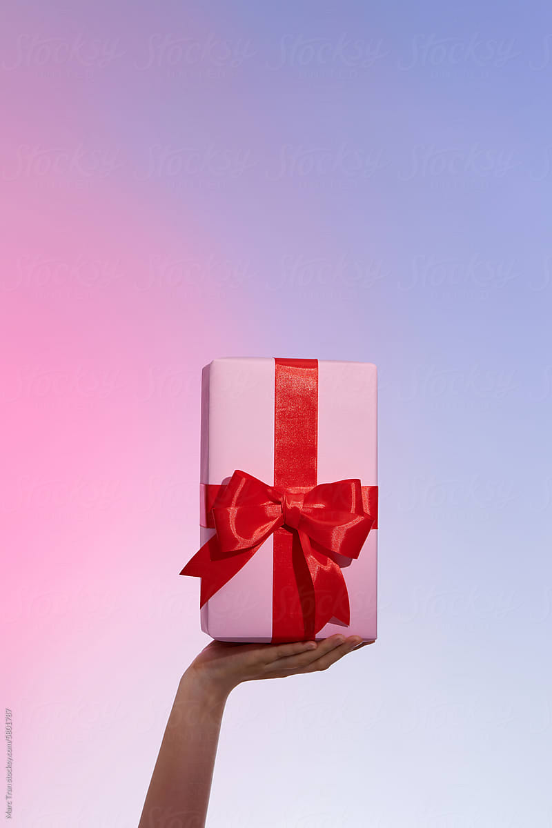Female hands hold a pink gift box with a red bow and slide it up