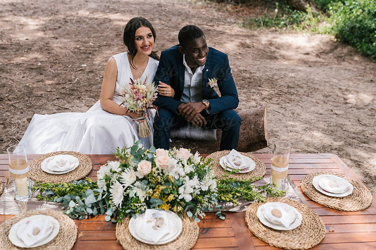 Joyful newlyweds seated at the wedding table in nature.