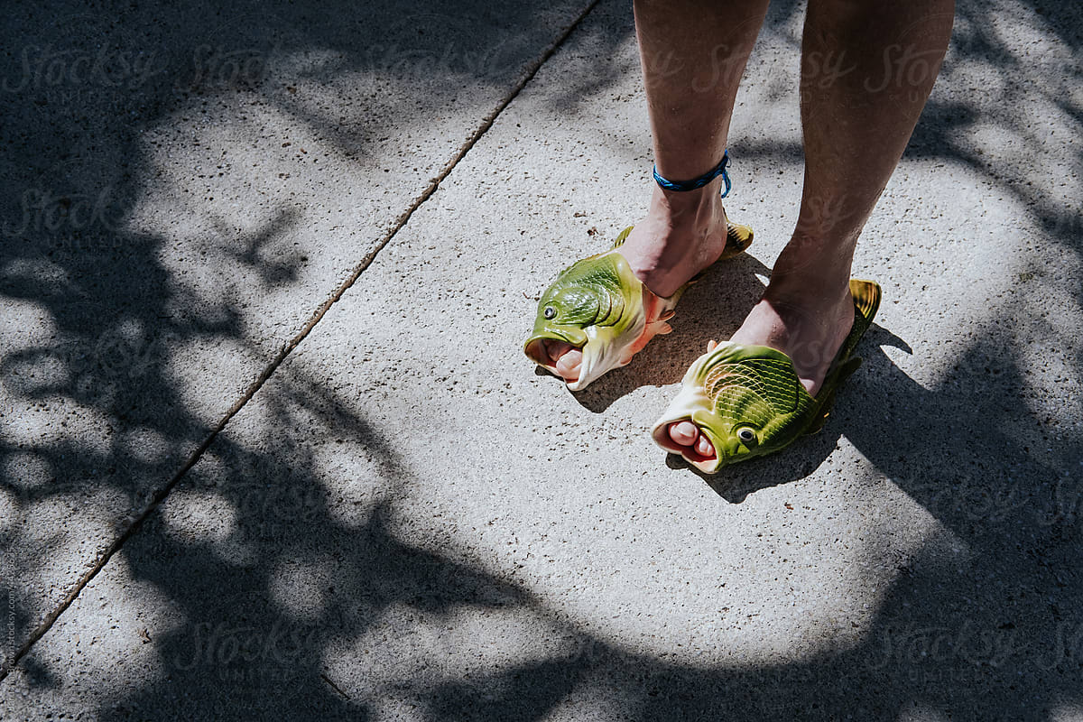 Man\'s legs wearing fish shaped sandals on the sidewalk.