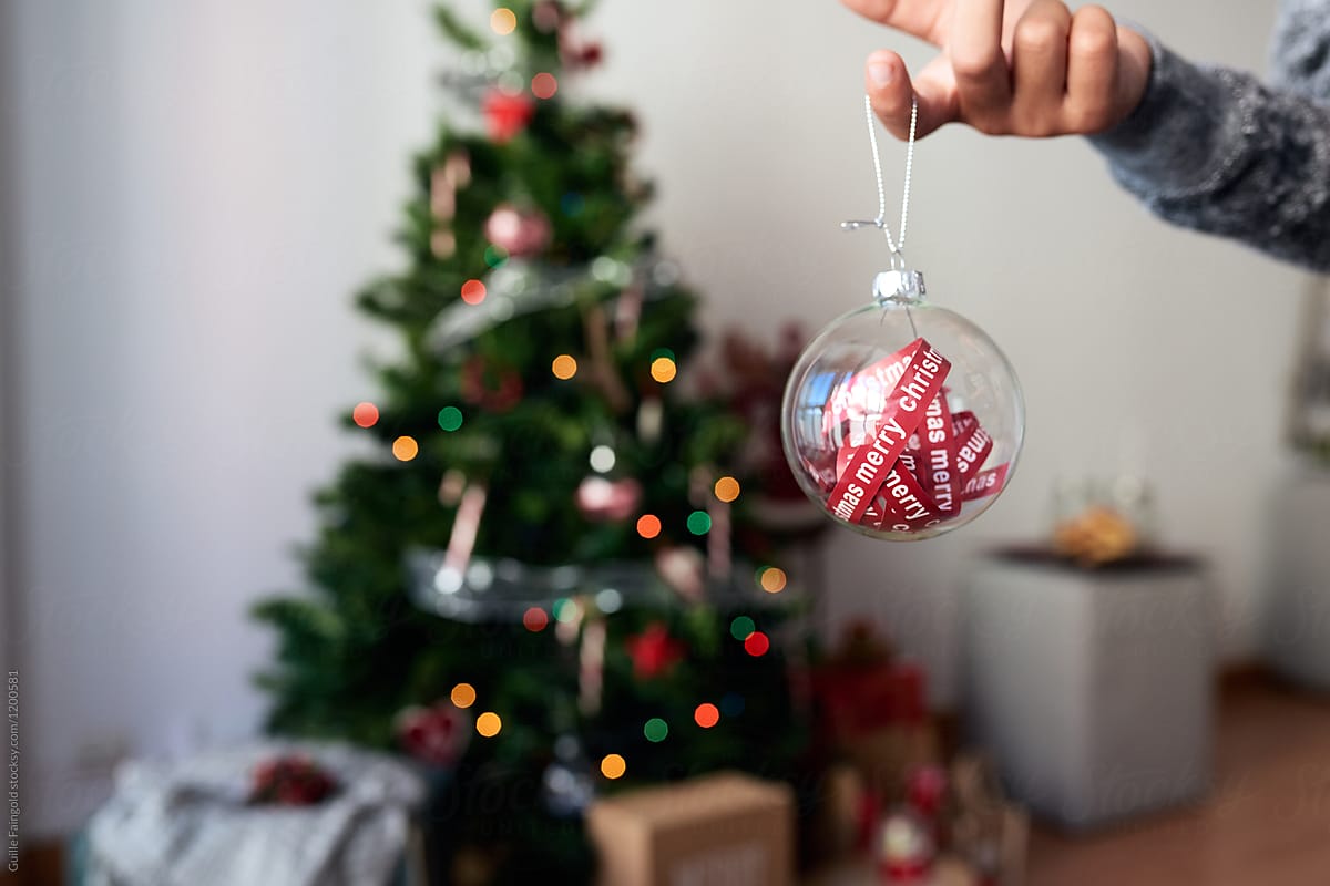 Kid holding Christmas ball with ribbons inside.