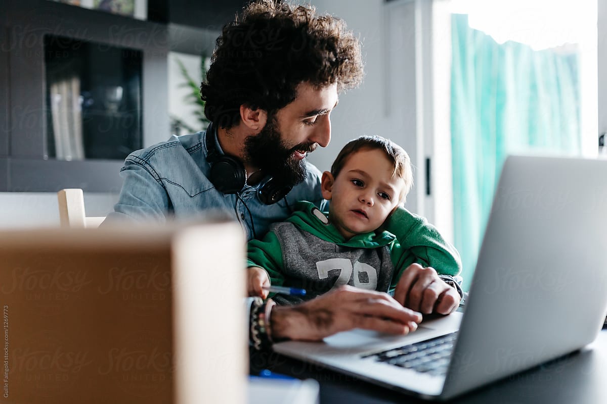 Smiling bearded father and bored son using laptop.